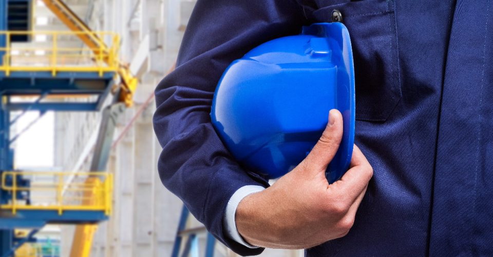 This picture is of a worker holding a hard hat under their right arm with an industrial setting in the background. This article discusses how safety consultants need to be adding value to their clients.